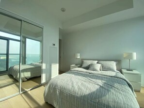 Een slaapkamer met een groot bed, twee nachtkastjes, een spiegel en een uitzicht door een glazen deur.