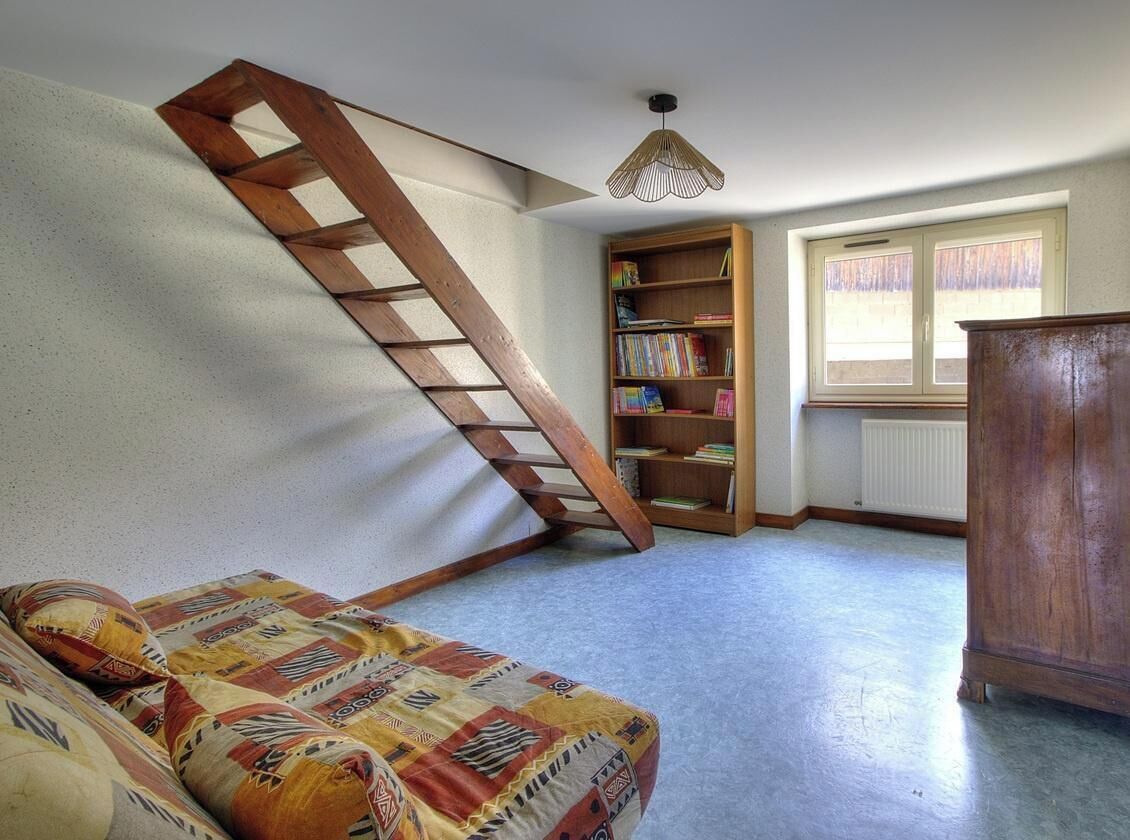 Et værelse med en trætrappe, en bogreol, en sofa og en radiator.