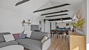 A modern living room with a grey sofa, a dining area with a wooden table, and a kitchen in the background. - Awesome home in Munkebo with house sea view (Munkebo)