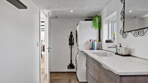 A modern kitchen with a built-in washing machine, a sink with a mirror, and a broom in the corner. - Awesome home in Munkebo with house sea view (Munkebo)