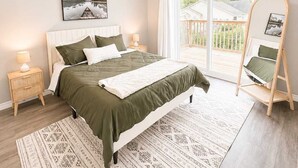 Une chambre à coucher avec un lit, une table de chevet, un fauteuil suspendu et une grande fenêtre.