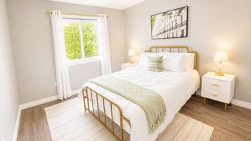 Quarto com cama, mesas de cabeceira, janela com cortinas, quadro na parede e tapete estampado.