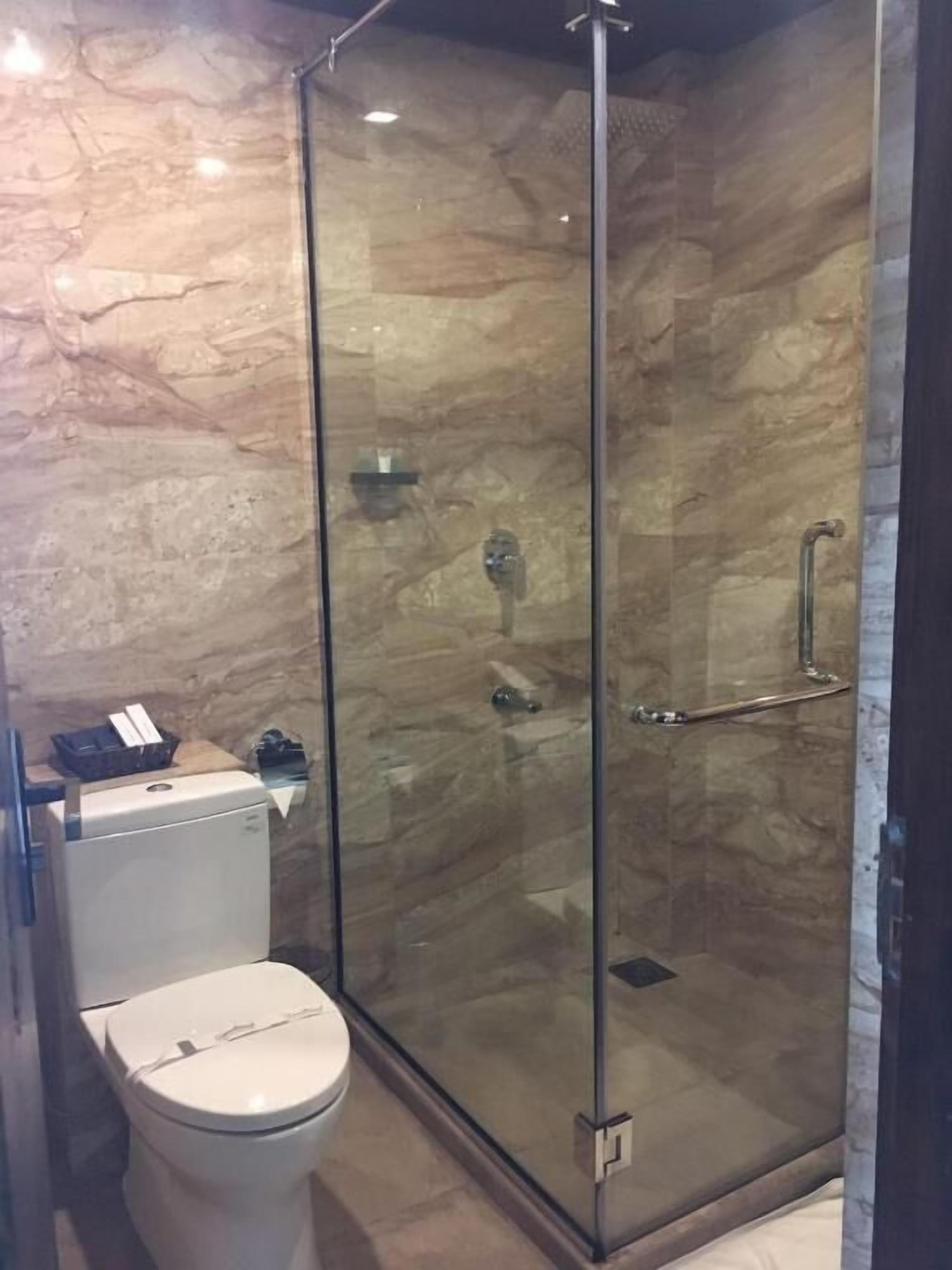 Kylpyhuone, jossa on lasiseinällä varustettu suihku, wc ja marmoriseinä.
