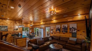 Interior de uma cabana de madeira com sala de estar, sala de jantar e cozinha.