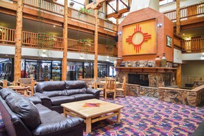 Eine großzügige Lobby mit Ledersofas, einem zentralen Kamin und einem Balkon mit Holzbalkonen.