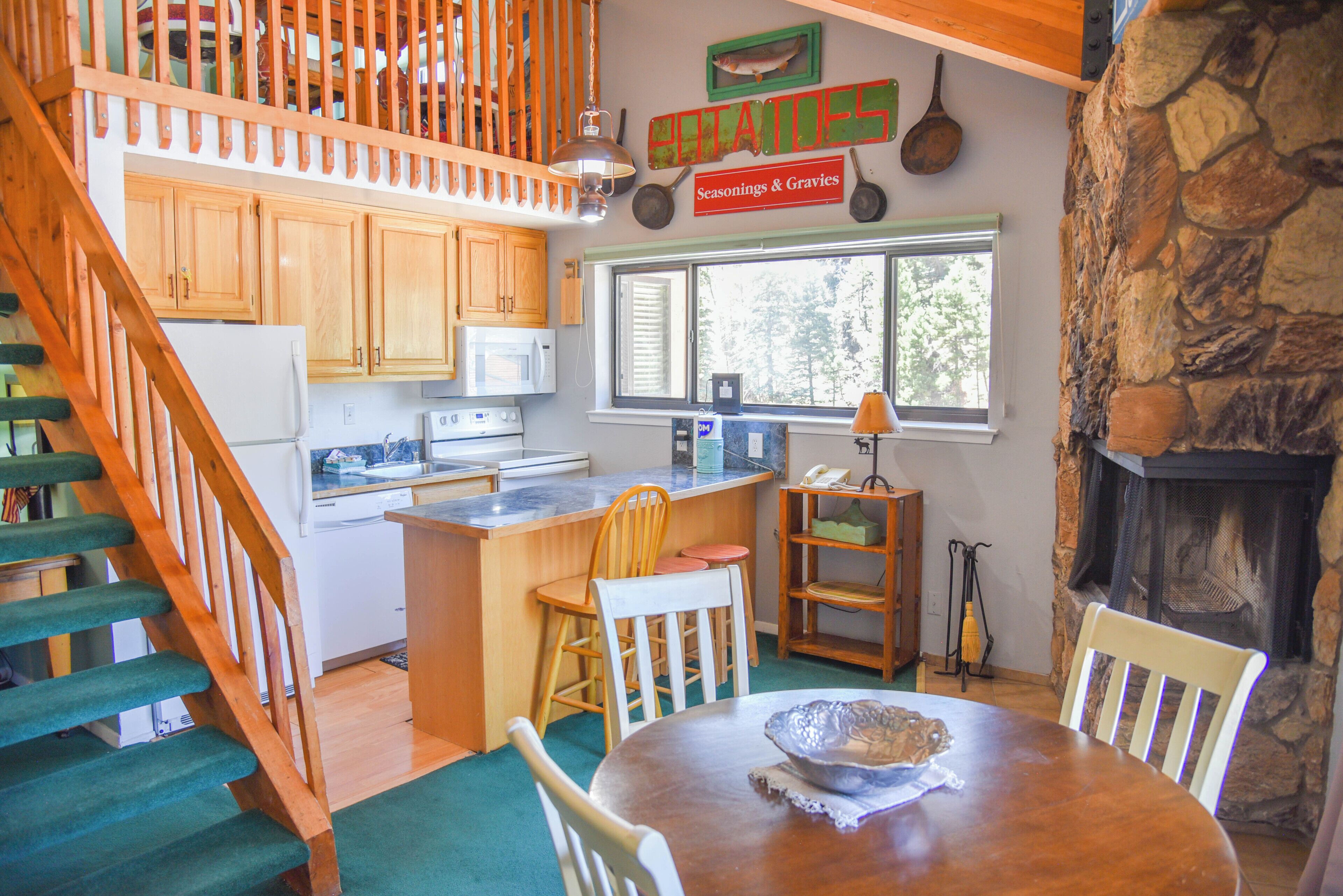 Une cuisine avec des meubles en bois, une cheminée en pierre et un coin repas comprenant une table et des chaises.