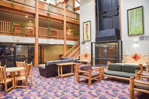 Eine geräumige Lobby mit hoher Decke, Holzmöbeln, einem gemusterten Teppich und einer Treppe zu einer oberen Etage.