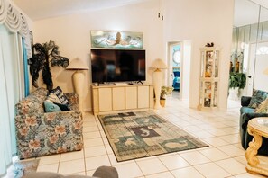 A living room with a sofa, TV, lamp, and decorative items. -  Three Palms 3BR / sleeps 8 / beach 5 min. / backs to nature trail & park w/lake (Largo)