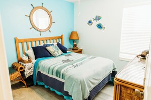 A bedroom with a wooden bed, a nightstand, a lamp, a wall mirror, and a window with blinds. -  Three Palms 3BR / sleeps 8 / beach 5 min. / backs to nature trail & park w/lake (Largo)