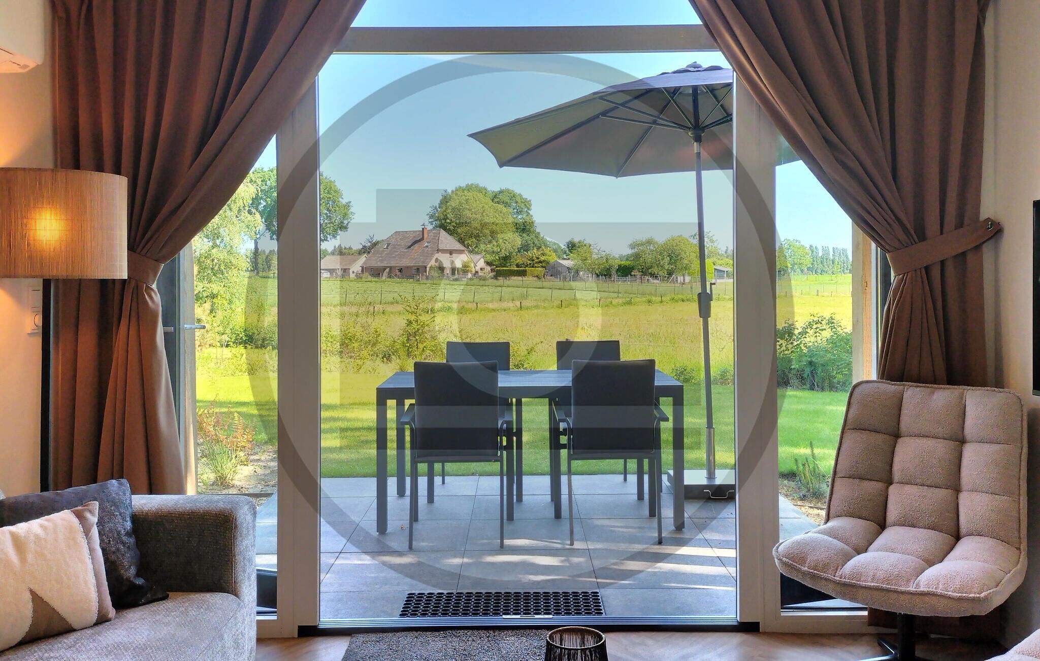 Une pièce dotée d’une porte vitrée donnant sur un patio extérieur, avec une table et des chaises, un fauteuil rembourré et une lampe.
