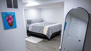 Een slaapkamer met een bed, een spiegel, een deur en een schilderij aan de muur.