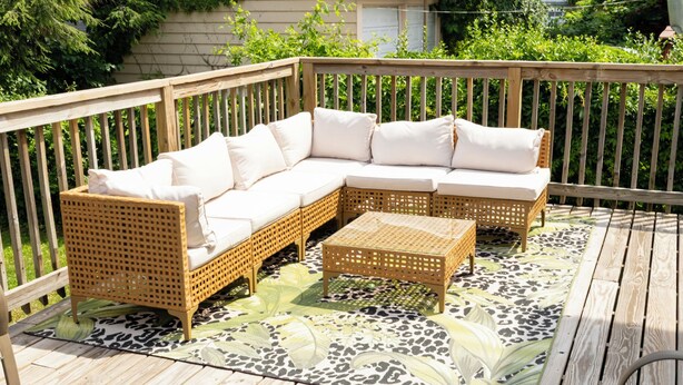 Een houten terras met een modulaire bank, een bijzettafeltje en een vloerkleed met een patroon.