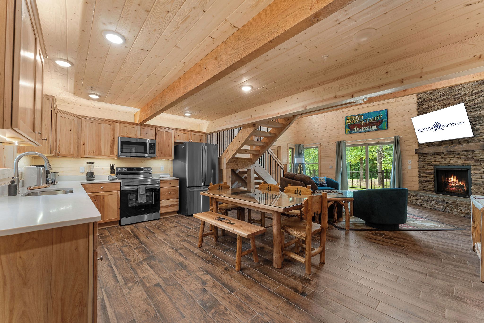 Una cocina amplia con electrodomésticos modernos, un comedor con mobiliario de madera, una chimenea de piedra y una escalera que conduce a un nivel superior.