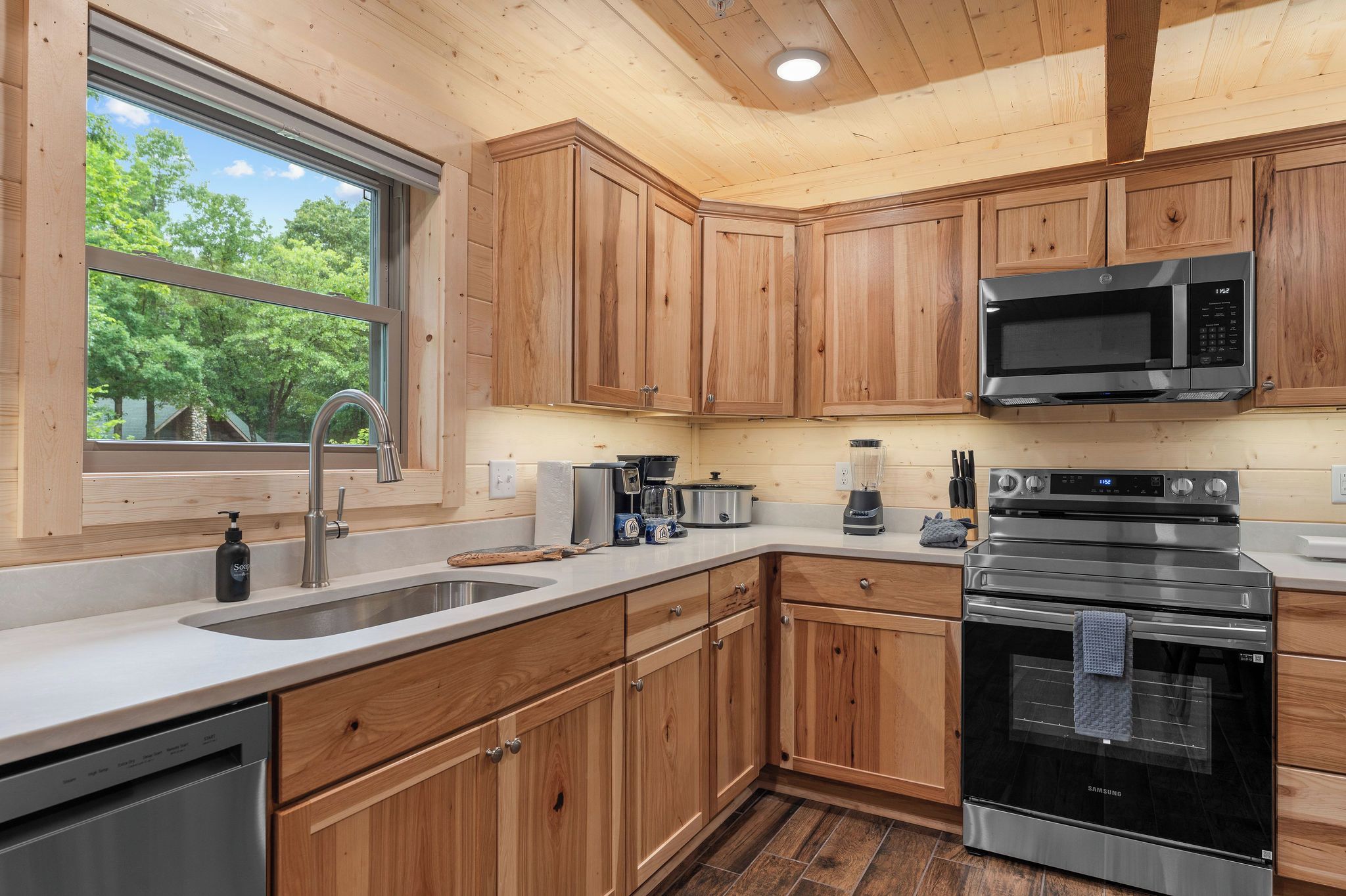 A modern kitchen with wooden cabinets, stainless steel appliances, and a large window.