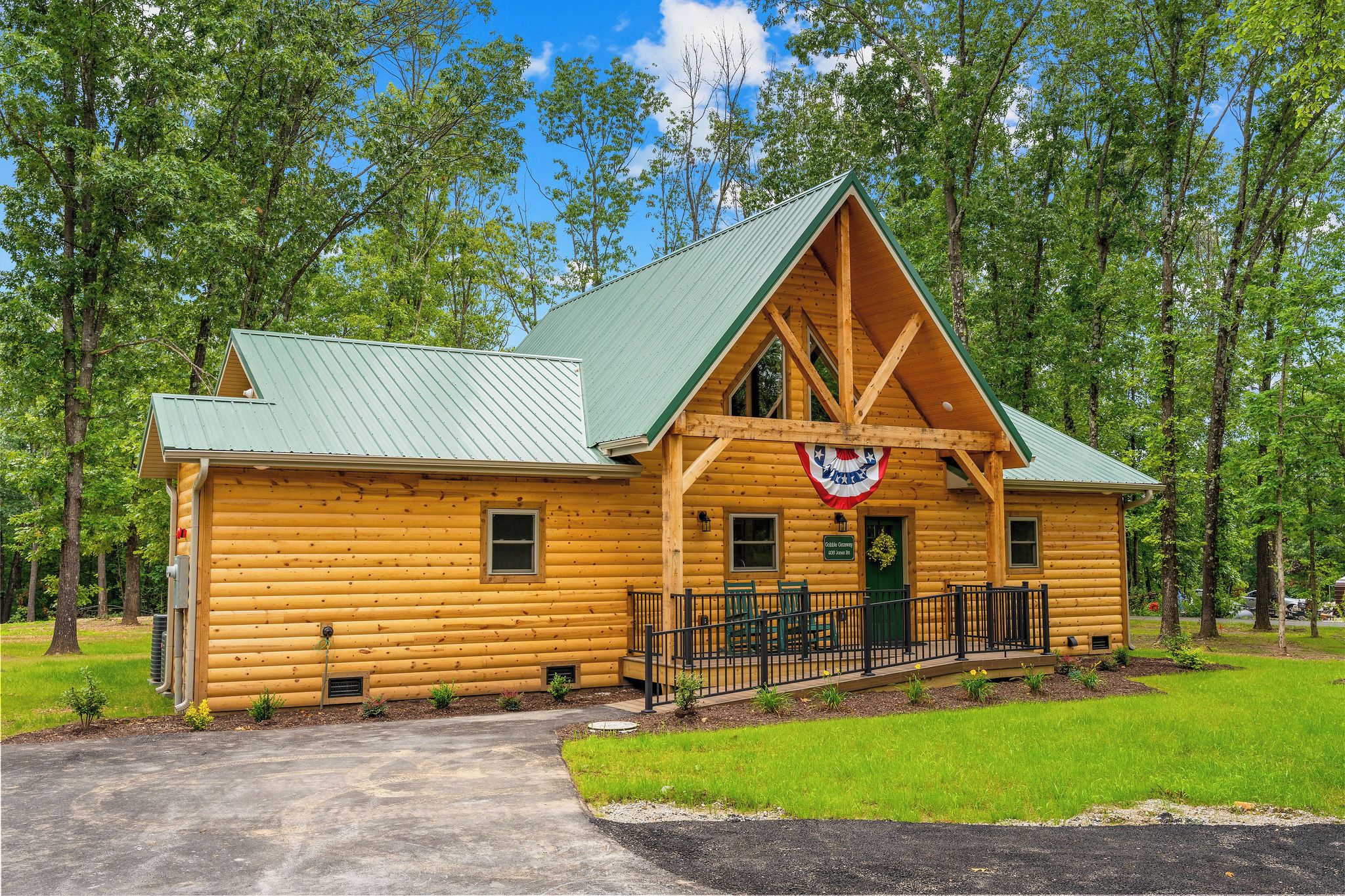 A log cabin with a green roof, a porch with a railing, and a flag.