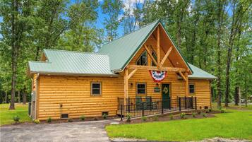 A log cabin with a green roof, a porch with a railing, and a flag.