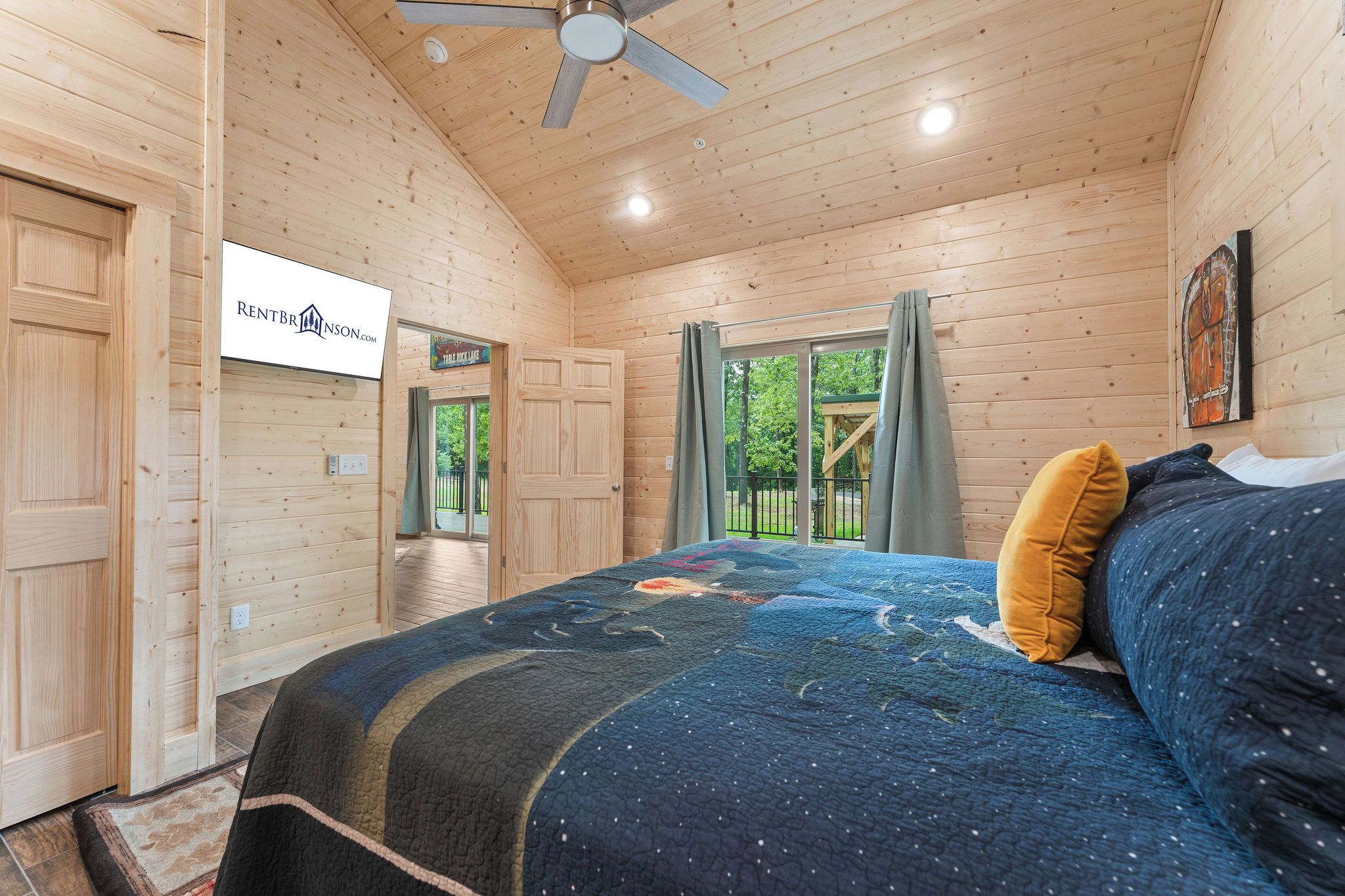 Een houten slaapkamer met een bed, een plafondventilator en uitzicht op buiten.