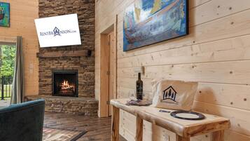 A cozy interior with a stone fireplace, wooden walls, a table with a bottle and glasses, and a painting on the wall.