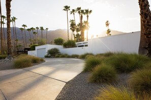 A modern building with a white facade, a garage, and a driveway leading to a gated entrance. - The Bond House | 37-Ft Salt Pool, Mosaic Spa, Fire Pit, Outdoor Shower, BBQ (Palm Springs)