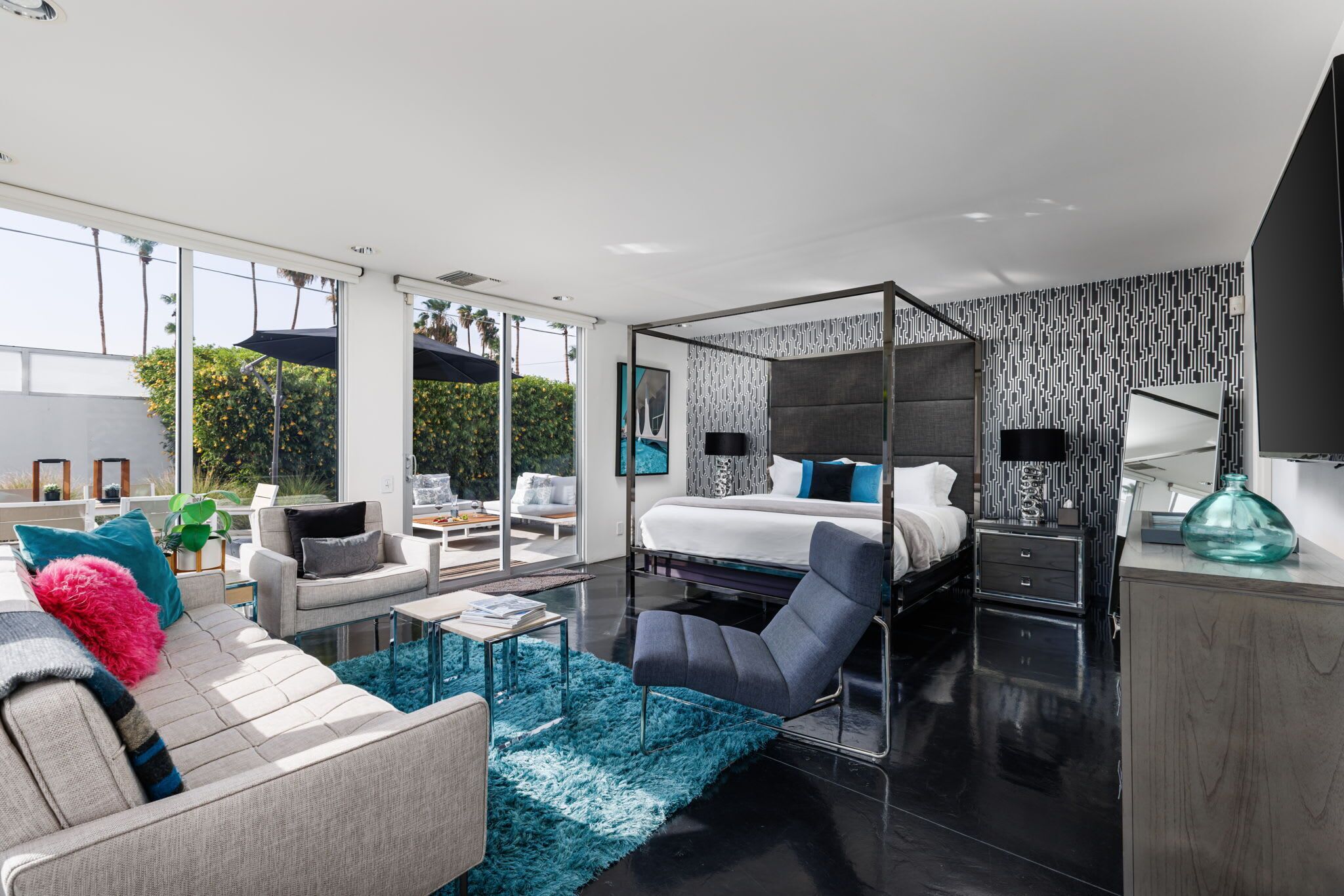 Una habitación de hotel moderna con una cama grande, una zona de estar con un sofá y sillones, una mesa de centro y vistas al exterior.