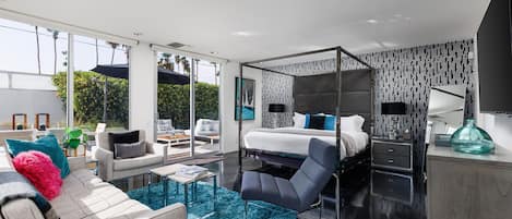 Una habitación de hotel moderna con una cama grande, una zona de estar con un sofá y sillones, una mesa de centro y vistas al exterior.