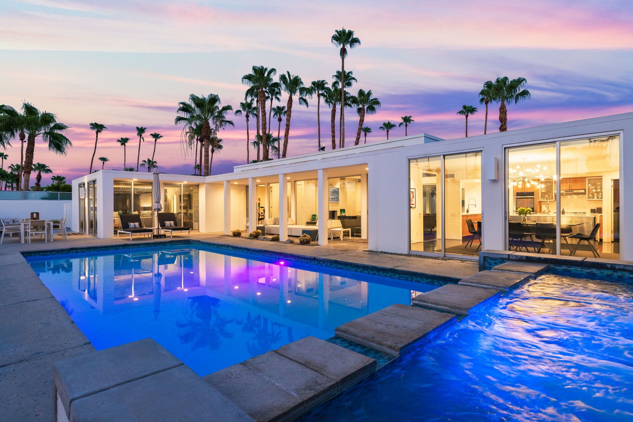 Un complexe hôtelier moderne doté d’une piscine, de palmiers et offrant une vue imprenable sur le coucher de soleil.