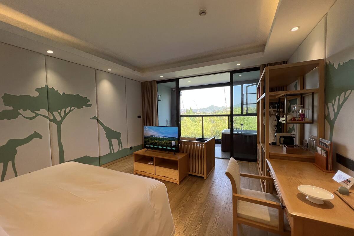 A hotel room with a bed, a TV, a desk, and a view of the outdoors.