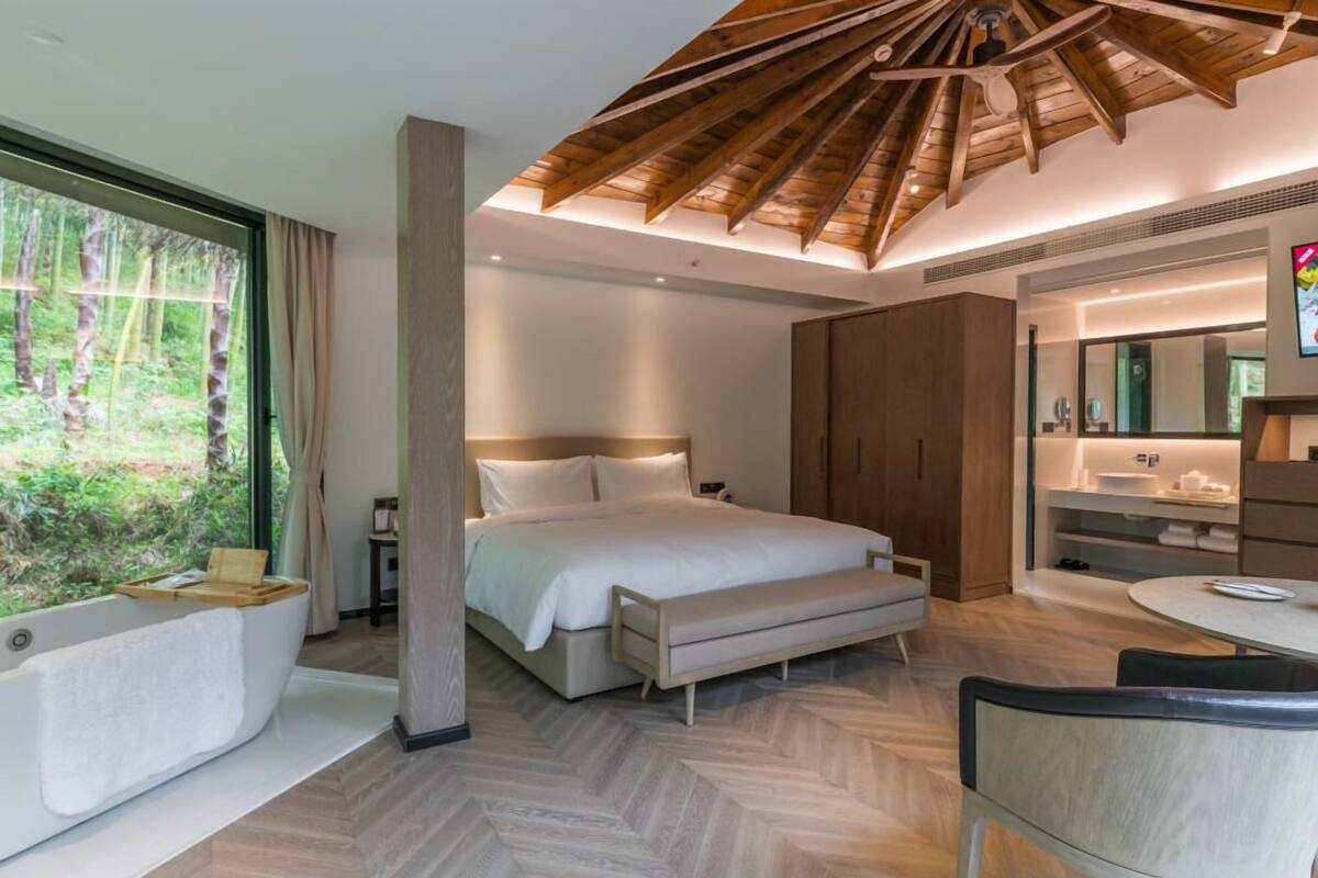 A modern bedroom with a large bed, a sitting area, a bathtub, and a dining area.
