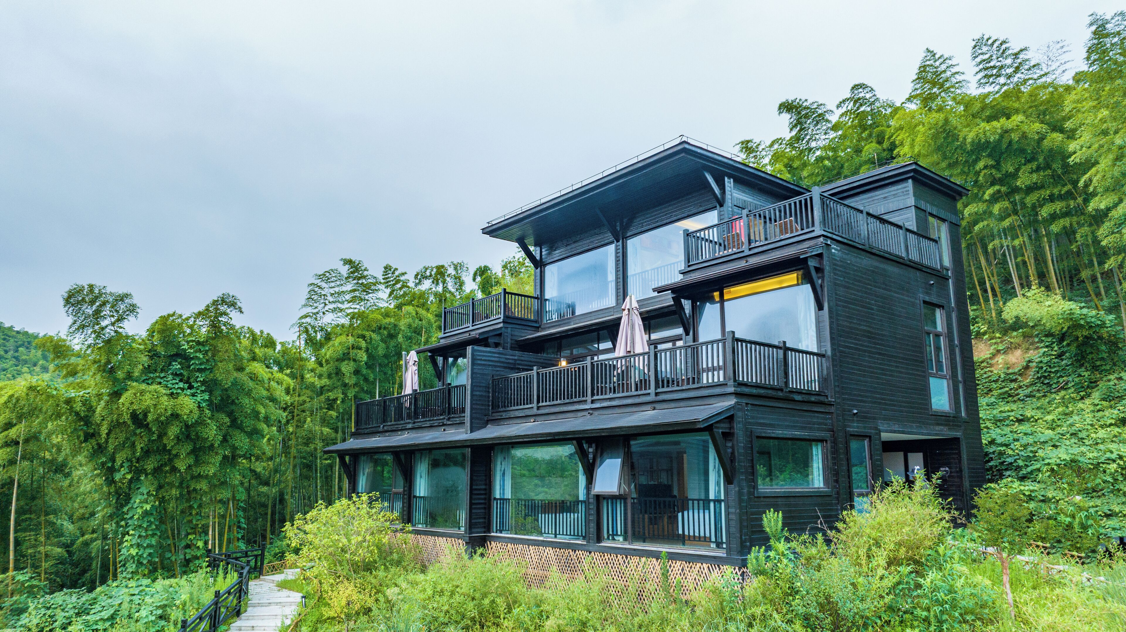 A multi-story wooden house with balconies, surrounded by dense forest.