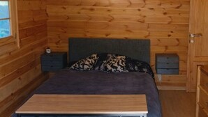 En stuga med träpanel, inredd med en säng, ett skrivbord och en stol.