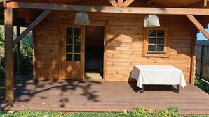 En stuga av trä med en veranda, ett bord med ett vitt duk och två fönster.