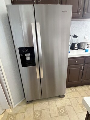 A stainless steel Whirlpool refrigerator with a water dispenser, located in a kitchen with patterned tile flooring and dark wooden cabinets.