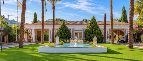 Un club de campo y golf con césped impecable, palmeras y un letrero que indica un límite de velocidad de 30 millas por hora.