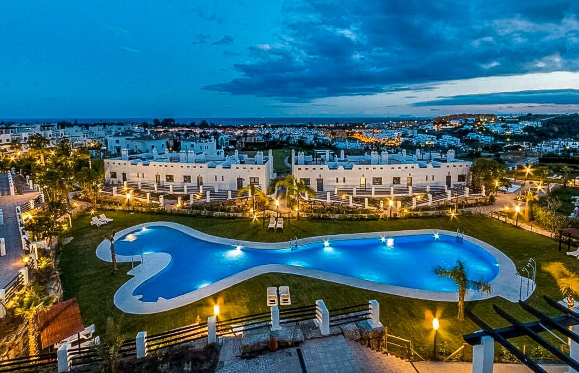 A resort with a large swimming pool, multiple guest rooms, and a view of the surrounding town.