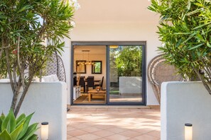 A modern interior with a dining area, a sofa, and a large sliding glass door leading to an outdoor space. - GuestReady - Sunset Golf with Private Garden (Estepona)