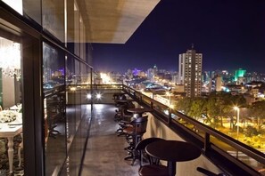A balcony with tables and chairs, a city view, and a building with illuminated windows. - Premium Room w/ Comfortable Bed & Steps to Chapecó’s Top Sights (Santa Catarina)