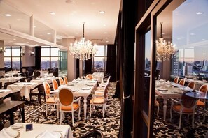 A dining area with tables set for service, large windows, and a city view. - Charming Space w/ Laqueada Wood Decor + “O Desbravador” Nearby (Santa Catarina)