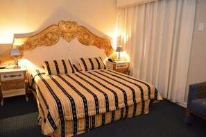 A hotel room with a large bed, two bedside tables with lamps, a blue armchair, and a decorative headboard. - Charming Space w/ Laqueada Wood Decor + “O Desbravador” Nearby (Santa Catarina)