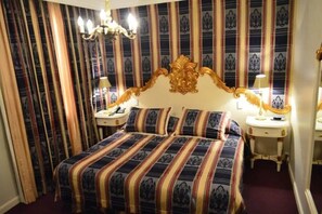 Ein Hotelzimmer mit einem großen Bett, einem verzierten Kopfteil, zwei Nachttischen mit Lampen und gestreiften Vorhängen.