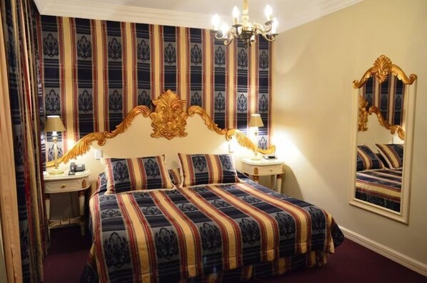 Ein Zimmer mit einem großen Bett, zwei Nachttischen, einer Chandelüster, einem Spiegel und gestreifter Tapete.