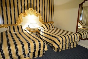 Ein Hotelzimmer mit zwei Betten, einem großen, verzierten Spiegel und einem Nachttisch mit Lampe.