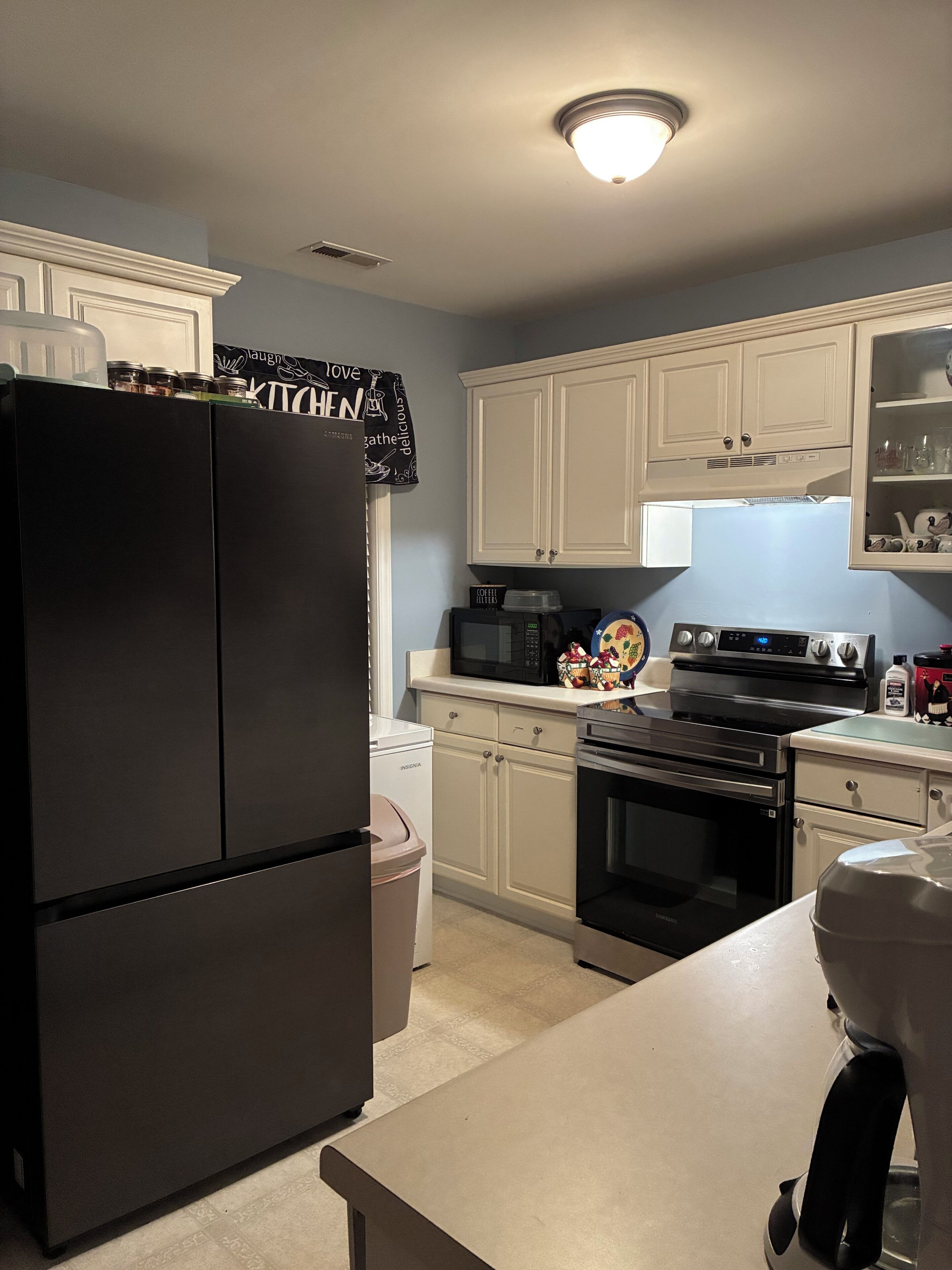 A kitchen with a black refrigerator, white cabinets, a microwave, an oven, and a countertop.