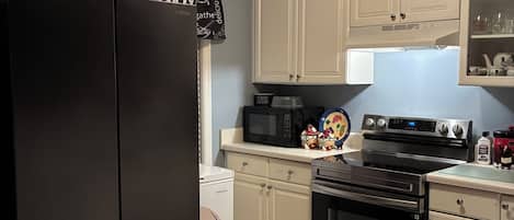 Una cocina con un refrigerador negro, gabinetes blancos, un microondas, un horno y una encimera.