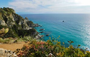Eine Küstenlandschaft mit freiem Blick auf das Meer, felsigen Klippen und einem Pfad, der zum Wasser hinaufführt.