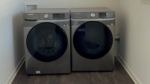 A laundry room with two Samsung washing machines, wooden flooring, and built-in shelving above the machines.