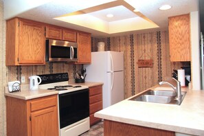 A kitchen with wooden cabinets, a stainless steel microwave, a white refrigerator, and a countertop sink. - Enjoyable 2-bedroom townhome with AC in Pinetop Country Club (Pinetop Country Club)