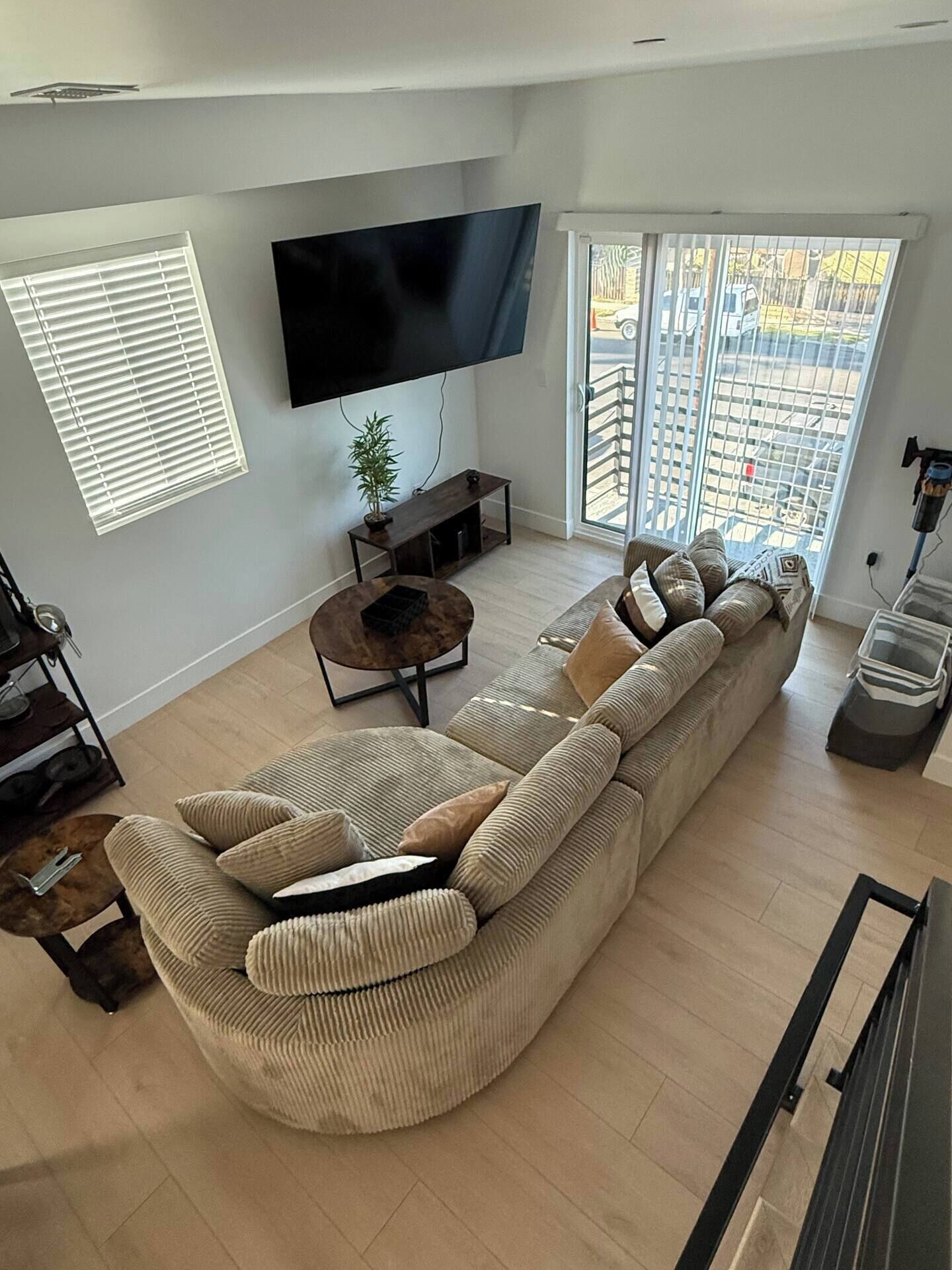 Un salon moderne avec un grand téléviseur à écran plat, un canapé d’angle, une table basse et une plante en pot.