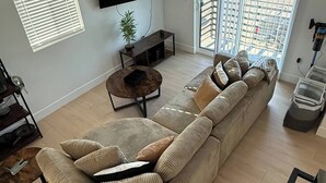 Uma sala de estar moderna com uma televisão de tela grande, um sofá em formato de L, uma mesa de centro e um vaso de planta.