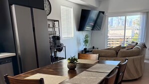 Uma cozinha moderna com uma mesa de jantar, cadeiras, um relógio e uma TV fixada na parede.