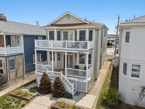 A two-story house with a balcony, a front porch, and a small front yard with two pine trees. - Family-Friendly 3BR/2BA OCNJ Getaway with Parking, Patios & Outdoor Shower (Ocean City)